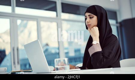 Shes young and ambitious. an attractive young arabic businesswoman working on her laptop in the office. Stock Photo