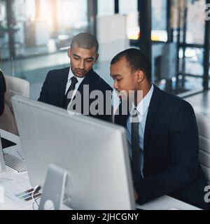 Putting their heads together. High angle shot of two corporate businessmen working together on a computer in the office. Stock Photo
