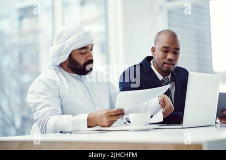 With solid teamwork, success is theirs for the taking. two businessmen using a laptop while having a discussion over paperwork in a modern office. Stock Photo