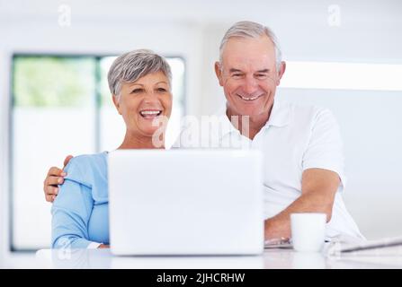 Happy mature couple using laptop. Happy mature couple smiling while using laptop at home. Stock Photo