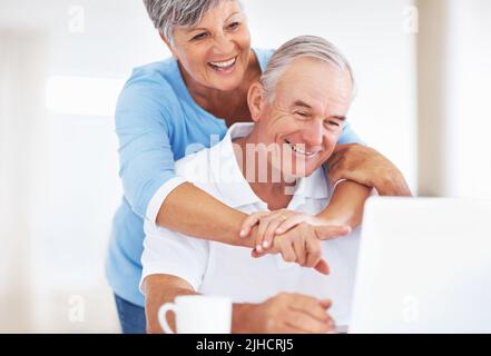 Loving mature couple using laptop. Loving mature couple smiling while using laptop at home. Stock Photo