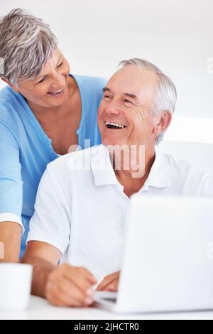 Couple with laptop enjoying time together at home. Cheerful mature man and woman enjoying time together at home while using laptop. Stock Photo