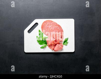 Meat food sausage salami slices on cutting board on black background, mocap. Copy space, flat lay Stock Photo