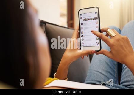 Closeup of woman on her smartphone lying on a sofa, relaxing in a bright living room. A young hispanic female relaxing and texting on her cellphone Stock Photo