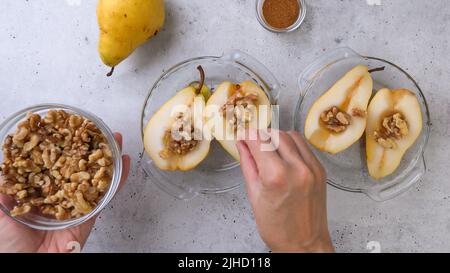 Baked pears with walnuts, honey, and cinnamon, close up on rustic background, perfect breakfast or dessert, flat lay, woman hands Stock Photo