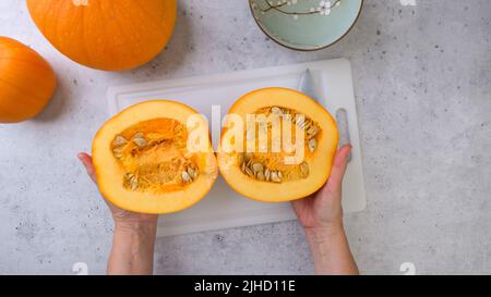 Woman cuts fresh ripe orange pumpkin into slices on grey stone background, flat lay Stock Photo