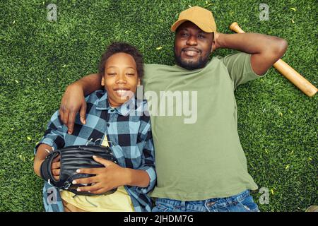 High angle view of father embracing his son while they lying on green grass and resting after baseball game Stock Photo