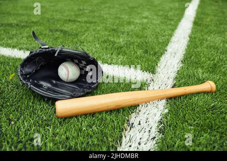 Close-up of baseball glove with ball and bat on green field preparing for baseball game Stock Photo