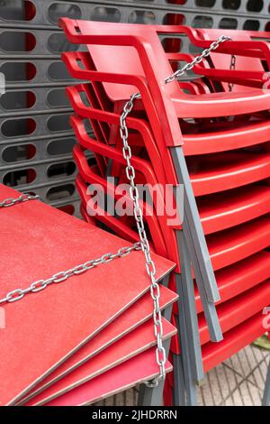 Chained red plastic chairs and tables of a closed cafe due to the lockdown. Street restaurant. Return of coronavirus concept Stock Photo