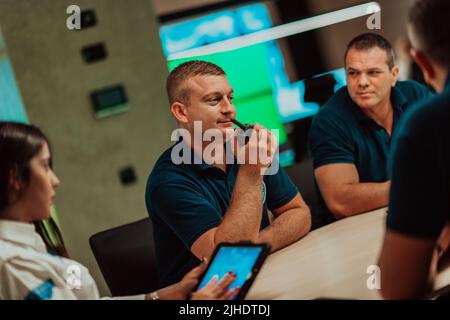 Group of security guards sitting and having briefing In the system control room They're working in security data center surrounded by multiple Screens Stock Photo