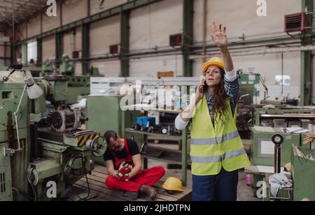 Woman is calling ambulance for her colleague after accident in factory. First aid support on workplace concept. Stock Photo
