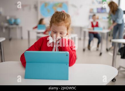 Bored schoolgirl using digital tablet during lesson in classroom at primary school. Stock Photo