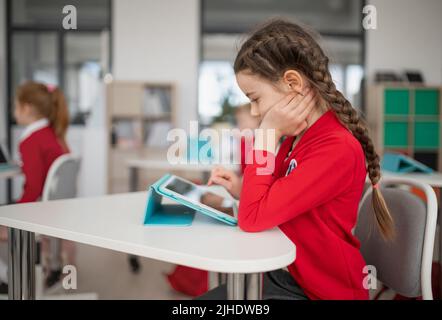 Schoolgirl using digital tablet during lesson in classroom at primary school. Stock Photo