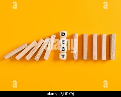 Wooden cubes with the word debt in line with the falling wooden blocks. Crisis, collapse and financial risk in business concept. Stock Photo