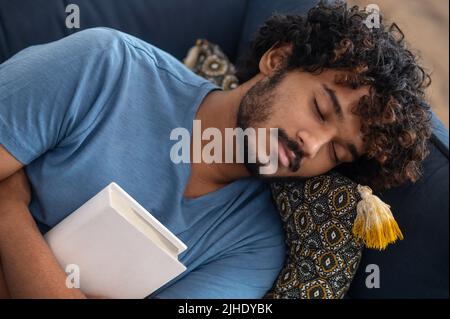 Young man sleeping on the sofa with a book in hands Stock Photo