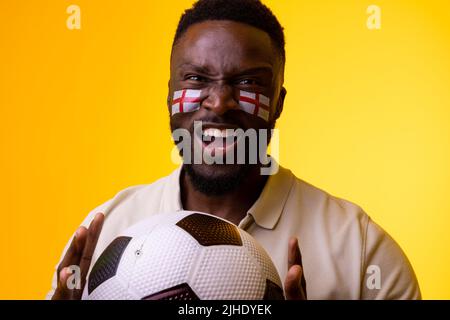 Image of african american male soccer fan with flag of england cheering in yellow lighting Stock Photo