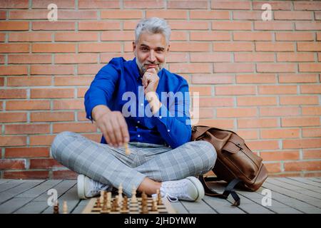 Successful happy businessman sitting in city street and playing chess. Stock Photo