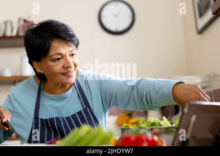 Low angle view of smiling biracial mature woman with short hair cooking food in kitchen Stock Photo