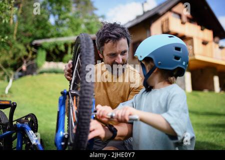Father with little son together preparing bicycle for a ride, pumping up tyres in garden in front of house. Stock Photo