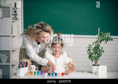 Schoolgirl drawing with teacher. Children from elementary school study ...