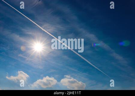 Blue sky with clouds and the sun, a white footprint from the plane Stock Photo