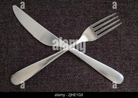 Crossed fork and knife on a gray tablecloth representing taking a break, silverware arranged in symbolic way on table, combination of neat ustensils Stock Photo