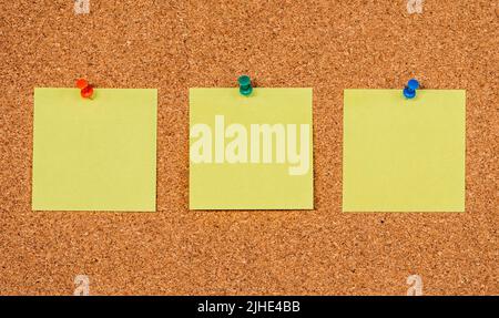 Three empty yellow sticky notes on a cork board with drawing pins, copy past Stock Photo