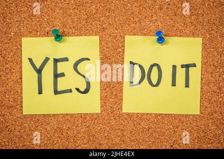 Yellow sticky notes on a cork board with drawing pin with the words Yes and Do it Stock Photo