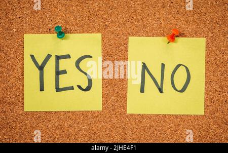 Yellow sticky notes on a cork board with drawing pins with the words Yes and No Stock Photo