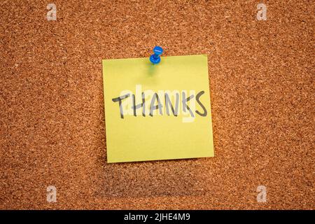 Yellow sticky note on a cork board with drawing pin with the word Thanks Stock Photo