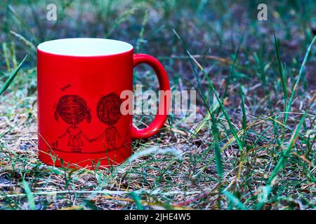 Red ceramic cup inscription love and funny couple on green grass in the park Stock Photo