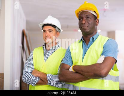 Portrait of two positive builders standing in construction site Stock Photo
