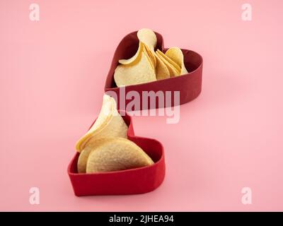 Chips in a box in the shape of a heart on a pink background. Chips in a box on a pink background. Stock Photo