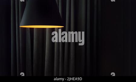 Close-up on a modern lamp against the background of the folds of curtains in dark colors with copy space Stock Photo