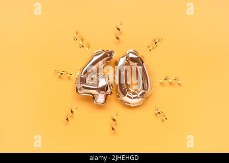Number 40 air balloons with ribbon confetti on a gold colored background. Stock Photo