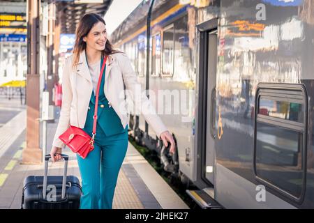 Beautiful girl running and chasing the leaving train in station. Waving hand and rushing to get on - Young business woman with suitcase running Stock Photo