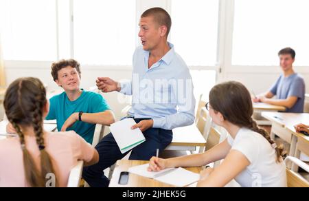 Male teacher working with teen students in classroom at school Stock Photo