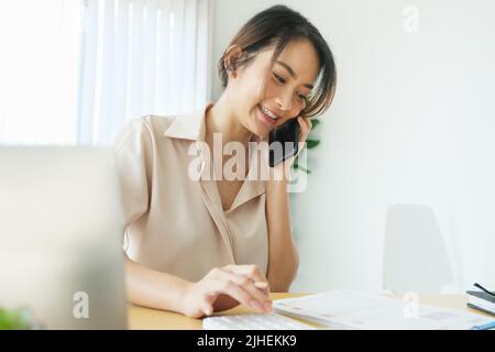 new normal, a businesswoman using computer and smartphone to work for a company Via the internet on your desk at home. Stock Photo
