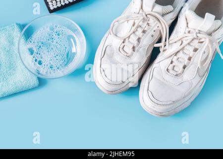 Dirty white sneakers with special tool for cleaning them on blue. Stock Photo