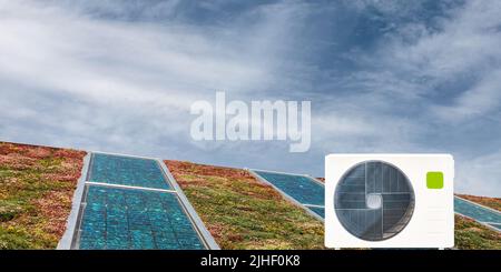 External heat exchanger of an air source heat pump in front of a sedum roof with solar panels Stock Photo