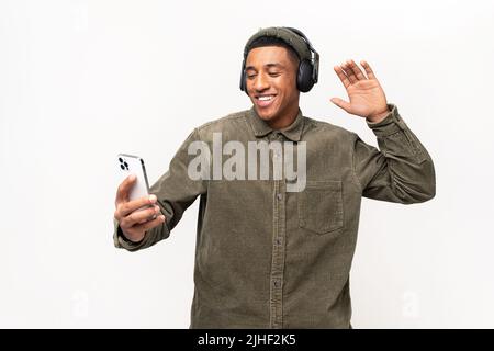 Ecstatic cheerful multiracial guy listening favourite tracks, dancing isolated on white. Joyful latin man wearing wireless headphones holding smartphone in hand, enjoying music Stock Photo