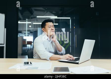 Asian man working in modern office, businessman having severe toothache, sick employee at work. Stock Photo