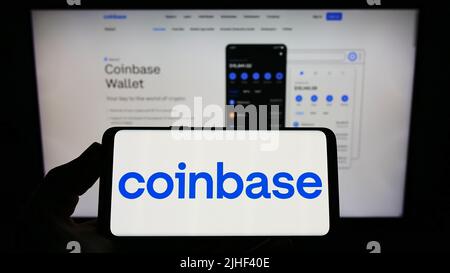 Person holding smartphone with logo of US crypto exchange company Coinbase Global Inc. on screen in front of website. Focus on phone display. Stock Photo