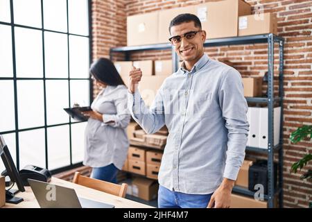 Young hispanic couple expecting a baby working at small business ecommerce smiling happy pointing with hand and finger to the side Stock Photo