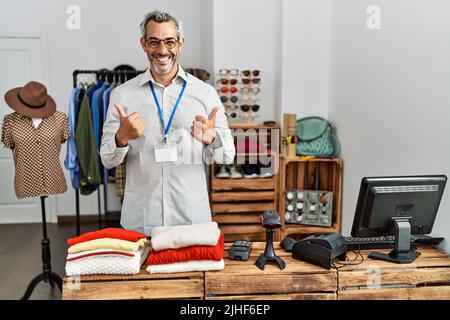 Middle age hispanic man working as manager at retail boutique success sign doing positive gesture with hand, thumbs up smiling and happy. cheerful exp Stock Photo