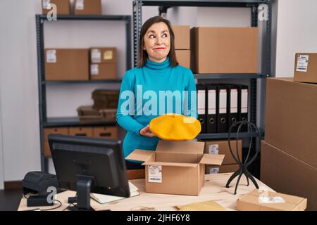Middle age hispanic woman working at small business ecommerce preparing order smiling looking to the side and staring away thinking. Stock Photo