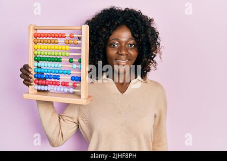 Young african american woman holding traditional abacus looking positive and happy standing and smiling with a confident smile showing teeth Stock Photo