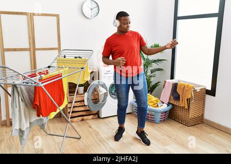 Young african man wearing headphones dancing at laundry room Stock Photo