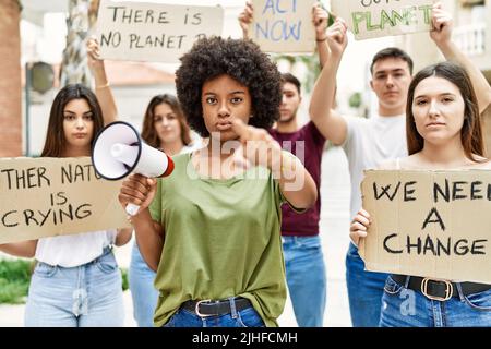 Group of young friends protesting and giving slogans at the street pointing with finger to the camera and to you, confident gesture looking serious Stock Photo