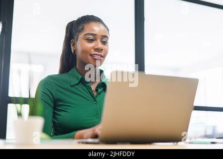 Portrait of a charming elegant young businesswoman sitting in the modern office in front of a laptop, female freelancer is enjoying work from coworking space Stock Photo